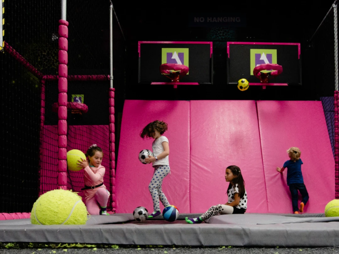 Young girls playing on a trampoline basketball hoop.